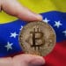 Hombre sosteniendo moneda de bitcoin frente a bandera de Venezuela. Composición por CriptoNoticias. erika8213 / elements.envato.com; wirestock / Freepik.com