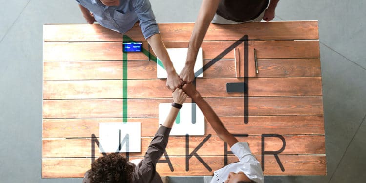 Grupo de trabajo juntando manos sobre mesa de Maker