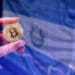 Pantalla con bandera de El Salvador y mano con bitcoin.