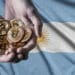 Bandera de Argentina y y mano sosteniendo bitcoins.