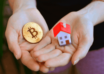 Unas manos sostienen una casa en miniatura y una moneda de bitcoin.
