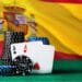 Dos ases de poker sostenidos por fichas de apuestas frente a la bandera de España.