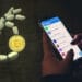 Una mano sosteniendo un bitcoin acompañado de un celular visualizando Telegram.