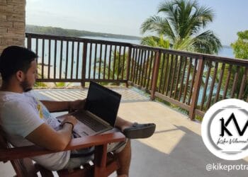 Hombre sentado con laptop en las piernas en el balcón de apartamento.