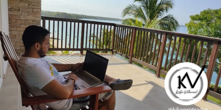 Hombre sentado con laptop en las piernas en el balcón de apartamento.