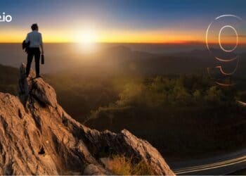 Hombre de negocios con una chaqueta de traje informal de pie sosteniendo una maletin de negocios en la cima de la montaña mirando el amanecer.