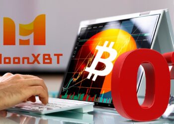 Las manos de un hombre escribiendo en un teclado inalámbrico conectado a una laptop con el logo de bitcoin en pantalla.