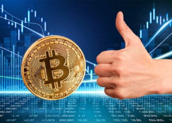 mano con pulgar arriba junto a moneda de bitcoin sobre superficie digital con gráfico de precio en el fondo