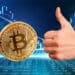 mano con pulgar arriba junto a moneda de bitcoin sobre superficie digital con gráfico de precio en el fondo