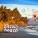 mano depositando moneda de bitcoin en playa con logo de Bitcoin Beach y bandera de El Salvador en el fondo