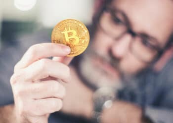 hombre sostiene moneda de bitcoin mientras la evalua