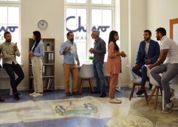 personas conversando en una sala con bandera de el salvador y onedas de bitcoin pintadas en el suelo, con logo de CHivo Wallet visible a traves de las ventanas