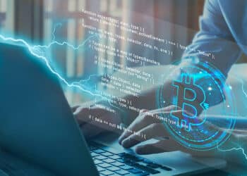 persona tecleando en computadora con logo de bitcoin y código proyectando desde la pantalla