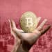 mano sostiene moneda de bitcoin con ciudad en rojo en el fondo