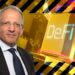 El vicegobernador del Banco de Inglaterra, Jon Cunliffe, en frente de señal de aviso con interfaz digital de defi en el fondo