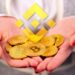 mujer sostiene monedas de bitcoin entre sus manos con logo de binance