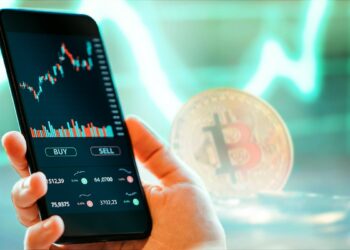 persona sostiene teléfono móvil con plataforma de exchange de criptomonedas en pantalla con bitcoin y gráfco de precio en verde en el fondo