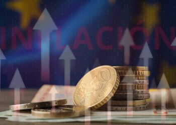 monedas de euros sobre mesa con flechas crecientes superpuestas y bandera de la comunidad europea en el fondo con "inflación" escrito