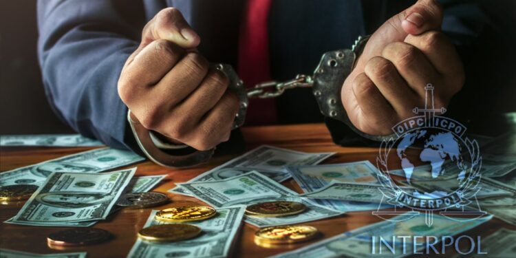 hombre esposado con monedas de bitcoin y billetes de dólares sobre mesa con logo de Interpol suerpuesto