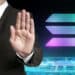 hombre muestra señal de rechazo con logo de Solana sobre platafoma digital en el fondo
