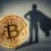 moneda de bitcoin proyectando sobre ade superheroe con logos de FTX en el fondo