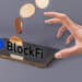 mano alcanzando telefono con logo de blockfi y criptomonedas