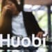 Logo de Huobi sobre escritorio con mujer empresaria con gesto de preocupación en el fondo