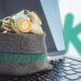 bolsa con logo de kucoin llena de criptomonedas sobre computadora con loo de kucoin en el fondo
