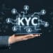 Mano de persona sosteniendo teléfono con gráficos y siglas KYC