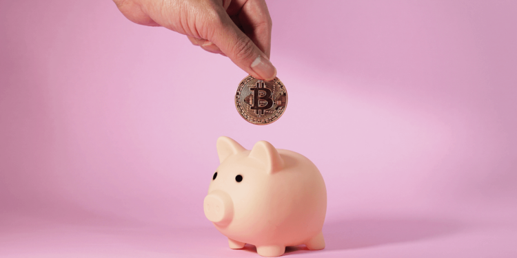 mano depositando monedad de bitcoin en alcancía de cochinito.