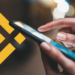 persona usando teléfono móvil con logo de Binance en el fondo