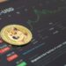 moneda de Dogecoin sobre pantalla mostrando grafico de precio en alza dentro de plataforma de trading