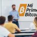 profesor dando clase a jovenes adultos con logo de Mi Primer Bitcoin en la pizarra