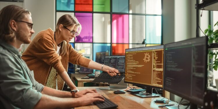programadores trabajando código en computadora con logo de bitcoin en pantalla
