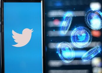monedas digitales con logo de twitter junto teléfono con la aplicación de twitter
