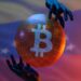 manos sosteniendo globo con logo de Bitcoin y bandera de Venezuela en el fondo