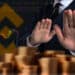 persona rechazando monedas apiladas con plataforma y logo de binance en el fondo