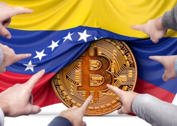 manos señalando moneda de bitcoin con bandera de venezuela