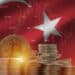 moneda de bitcoin entre pilas de monedas con bandera de Turquia con grafico de precio en el fondo