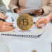 moneda de bitcoin sobre documento entre personas
