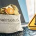 monedas de diversas criptomonedas en bolsa para prestamos sobre computadora junto a icono de advertencia