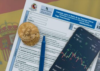 monedas de bitcoin y telefono movil con exchange de criptomonedas en pantalla sobre formulario de declaración de impuestos del gobierno de españa con bandera en el fondo