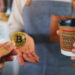 persona pagando con moneda de bitcoin café con logo de making coffee y bandera de el salvador en el fondo