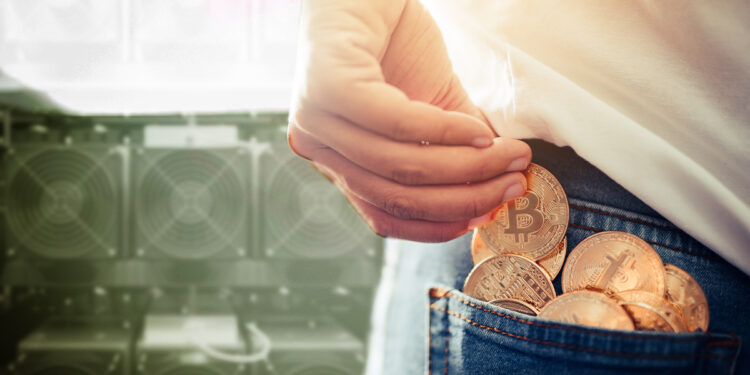 persona acumulando monedas de bitcoin en bolsillo de pantalón con mineros asic en el fondo