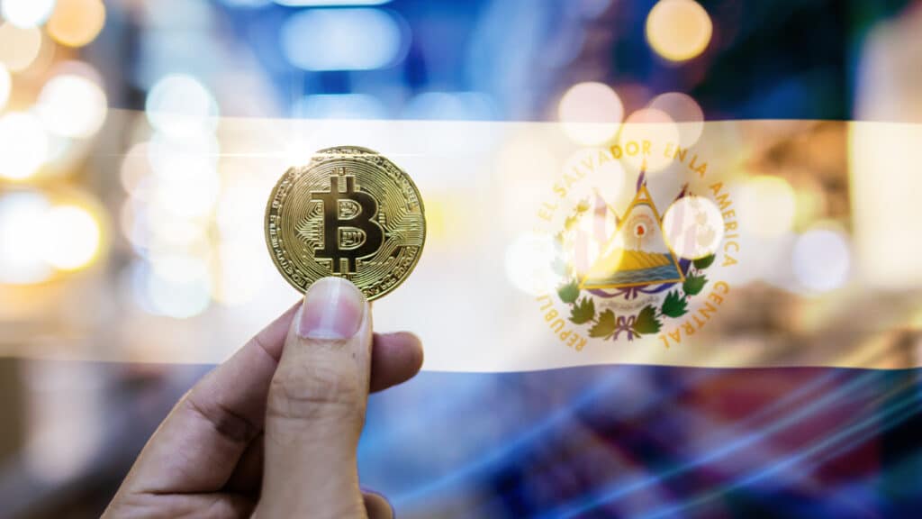 mano sostiene moneda de bitcoin con bandera de El Salvador en el fondo