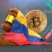 Martillo de ley junto a bitcoin y bandera de Colombia. De fondo un exchange.