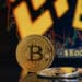 moneda de bitcoin junto a ventala señalando 5.000 dólares menos de precio con grafico de precio y logo de Binance en pantalla al fondo