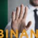 hombre haciendo señal de pare con la mano a logo de binance con bandera de Nigeria en el fondo