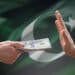 mano rechazando a mano ofreciendo billetes de dolares con bandera de pakistan en el fondo