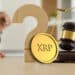 moneda de XRP de Ripple entre signo de interrogacion y martillo de juez sobre escritorio legal con persona en el fondo
